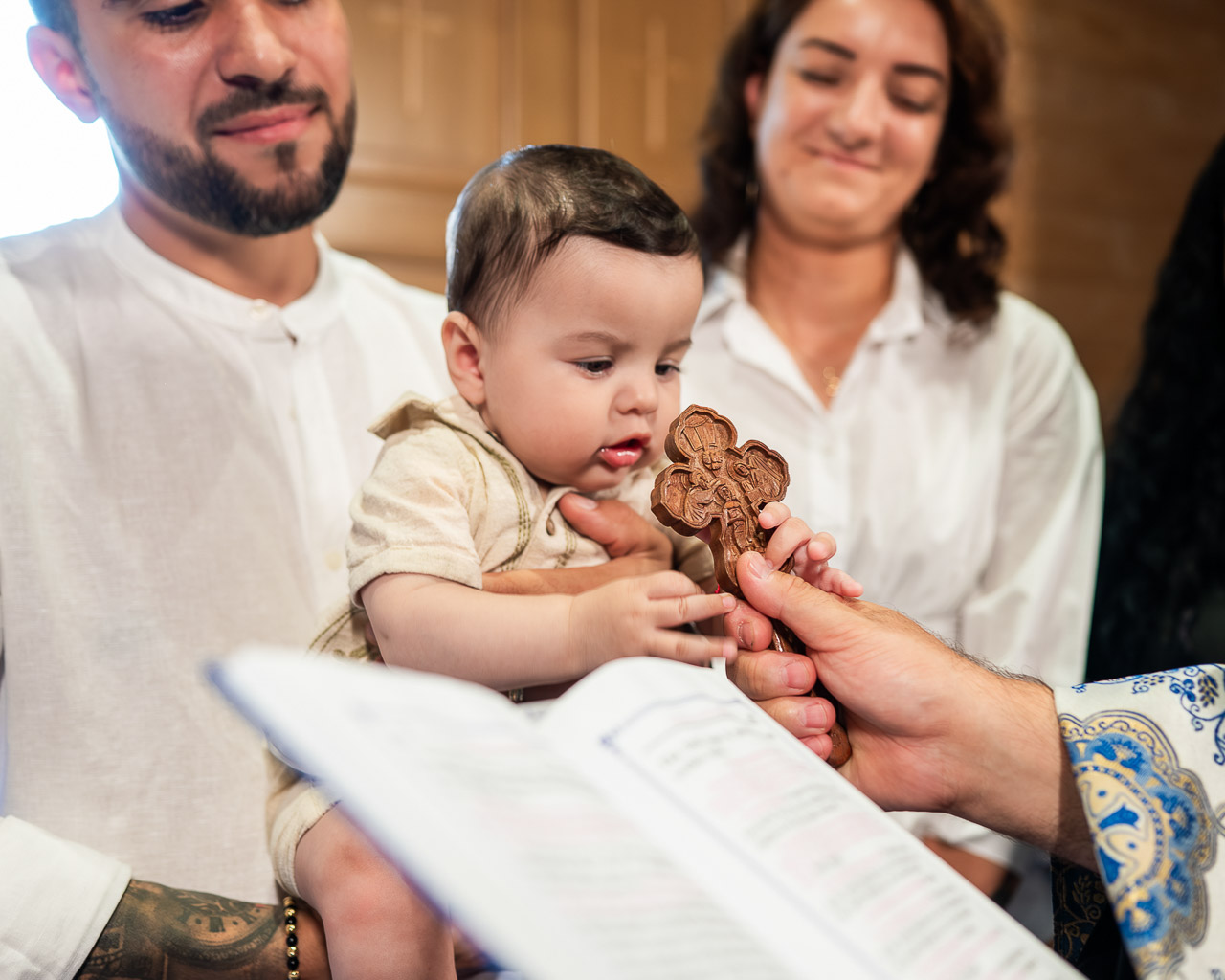 Fotograf botez Bucuresti – bebeluș atinge crucea, momentul binecuvântării alături de familie